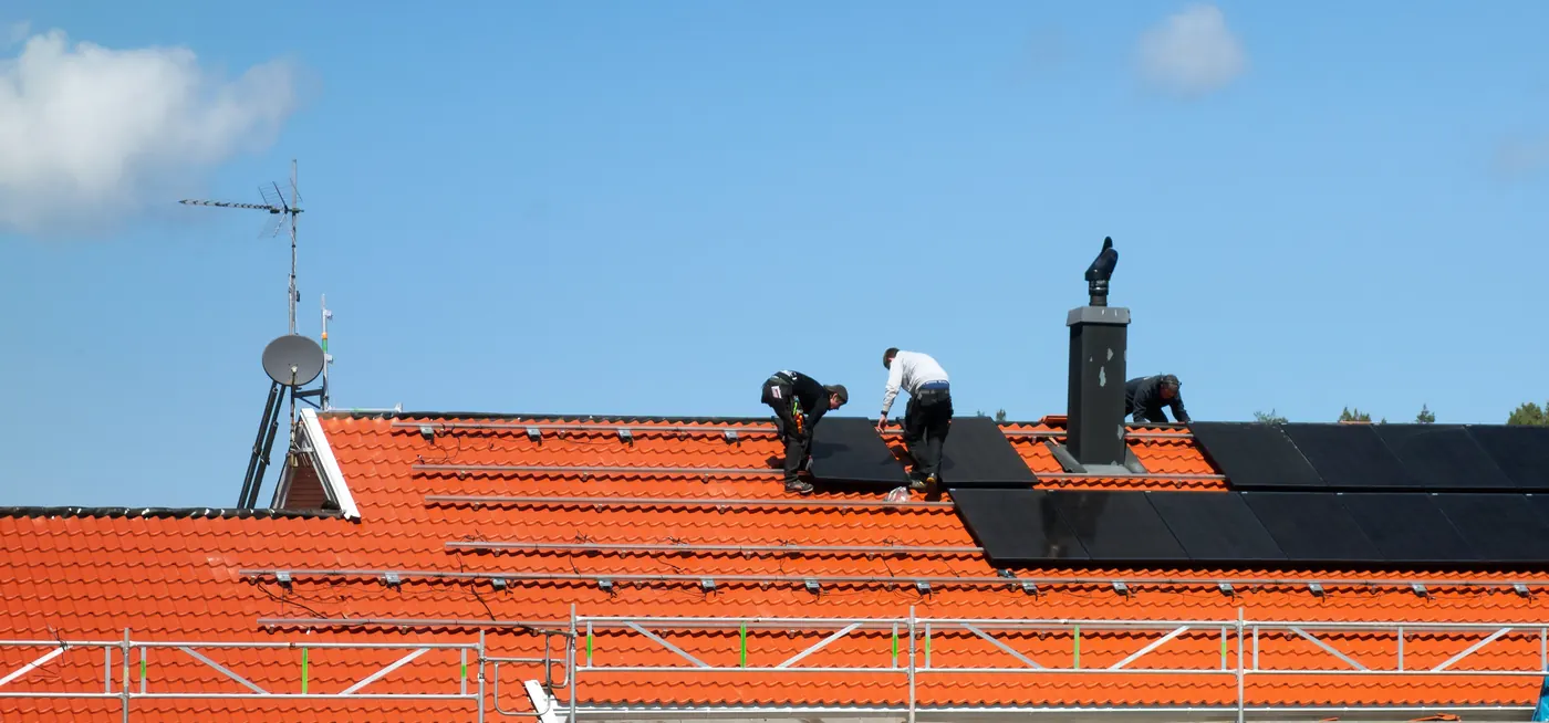 Trois installateurs posent des panneaux solaires photovoltaïques noirs sur une toiture en tuiles