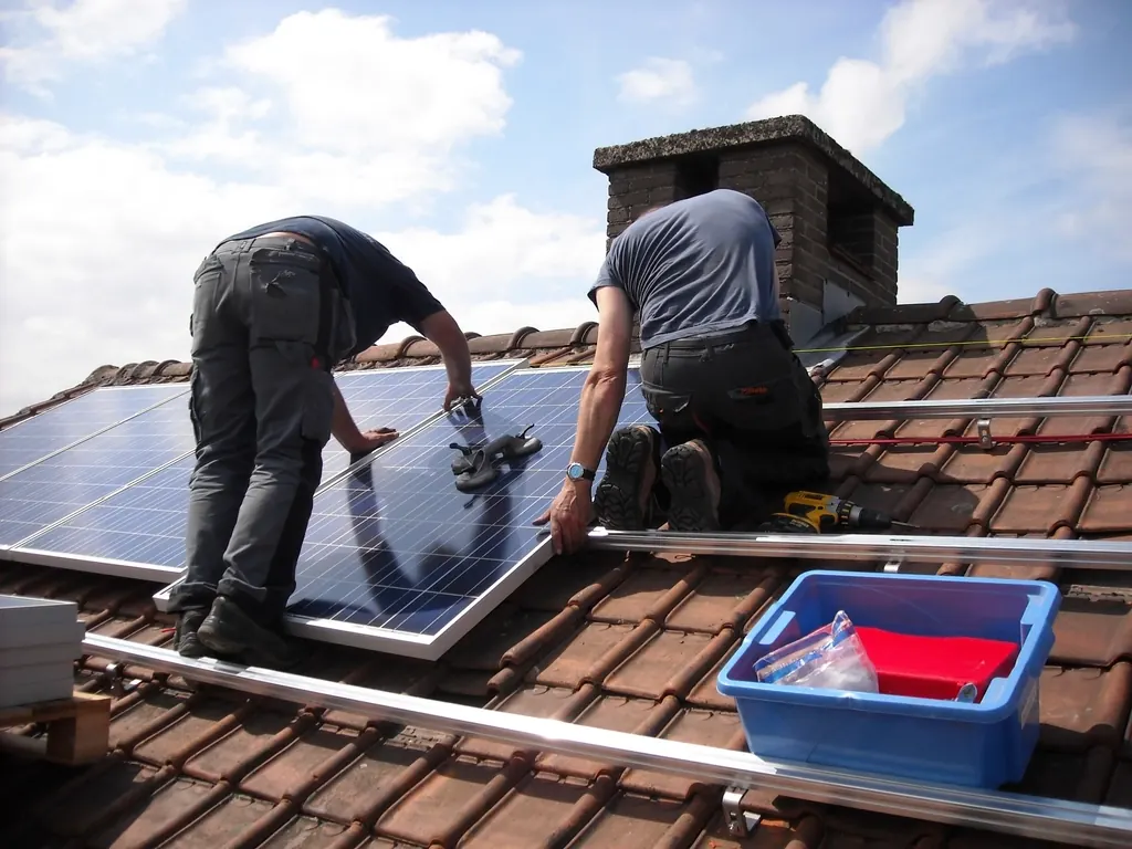 Deux installateurs fixent un panneau photovoltaïque sur les rails d'un toit en tuiles
