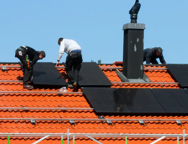 Installateurs posant des panneaux solaires noirs sur un toit en tuiles orange